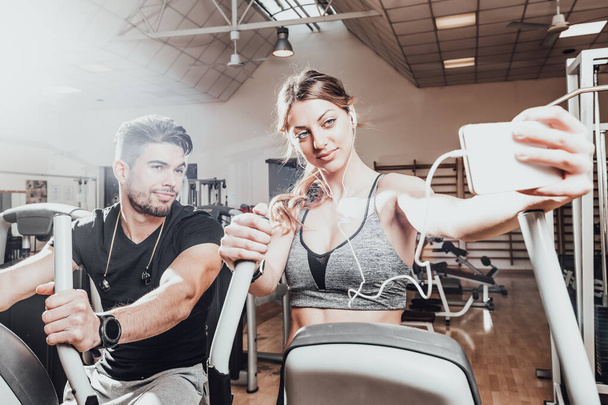 Smiling couple talking a selfie at gym. Young men and women in sportswear taking selfie at fitness club. Close u - Photo, Image
