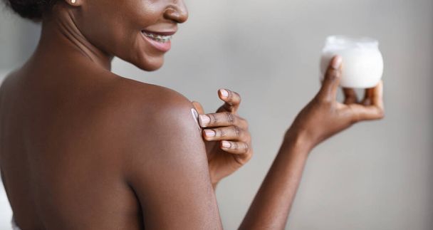 Нерозпізнавана афріканська жінка, яка застосовує масло для шкіри на плечі. - Фото, зображення