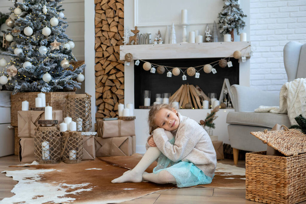 A child on the background of a Christmas tree, gift boxes and a decorative fireplace - Фото, зображення