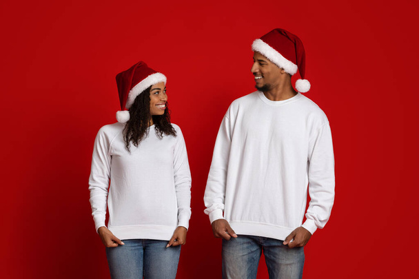 Uśmiechnięty mężczyzna i kobieta w białych swetrach i kapeluszach Mikołaja - Zdjęcie, obraz