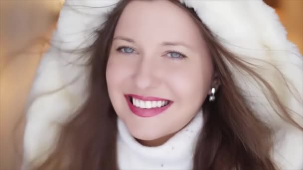Moda de invierno y look navideño. Hermosa mujer sonriente con suéter blanco y abrigo de piel esponjosa con capucha envuelta como retrato de Navidad - Metraje, vídeo