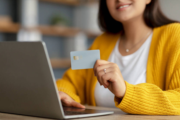 Pago sin efectivo. Mujer árabe sosteniendo la tarjeta de crédito y escribiendo en la PC portátil, compras en línea desde casa, primer plano, recortado - Foto, Imagen