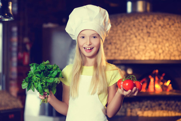 Little girl dressed as a cook with vegetables in her hands. - 写真・画像