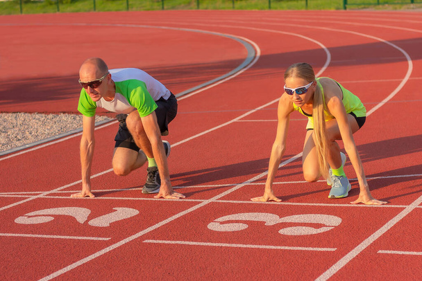 Atletická žena a muž na trati stadionu se připravuje na start, začíná běhat. koncepce sportu, tréninku a zdravého životního stylu, soupeření a rovnosti mezi pohlavími. - Fotografie, Obrázek