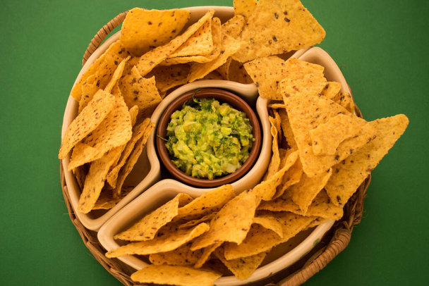 Some fried nachos in a pot with some fresh guacamole on a green surface  - Fotoğraf, Görsel