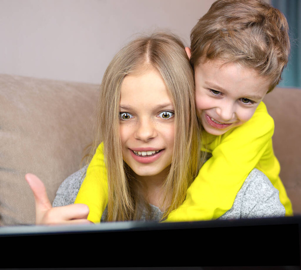 Children communicate on a laptop online. The boy hugs the girl and smiles. Online communication concept - 写真・画像