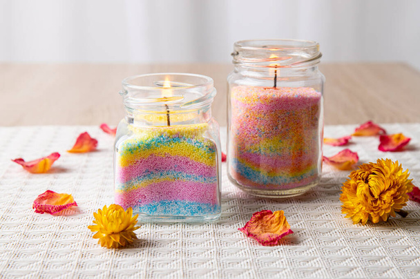 Children made fun colorful layered wax powder candles in home by pouring powder in old baby food jar and inserting wick inside, minimal background. Hobby concept. - Photo, Image