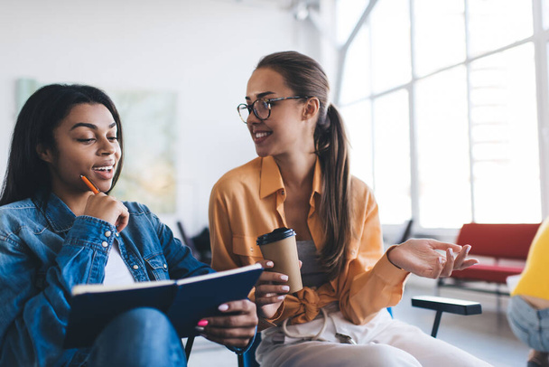 Multiracial businesswomen watching something in notebook and talking. Concept of modern successful women. Idea of teamwork. Young european and black girls in office. Caucasian woman with coffee - Foto, immagini