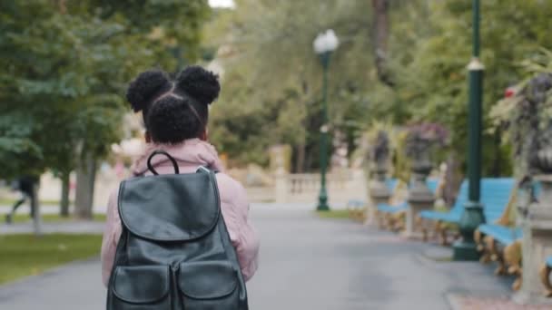 Visszapillantás kis afro-amerikai lány afro-amerikai gyerek fekete gyerek hátizsák fut siet az iskolába. Oktatási koncepció. Kisiskolás lány diák fut a szabadban a városi parkban megy az osztályba óra után - Felvétel, videó