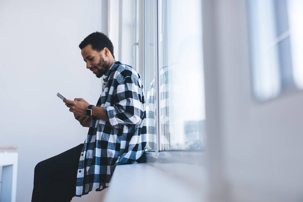 Millennial člověk chatování v sociálních sítích pomocí 4g bezdrátové na moderní mobilní gadget, mladistvý hipster chlap čtení webové publikace procházení stránky na mobilní technologie během volného času uvnitř - Fotografie, Obrázek