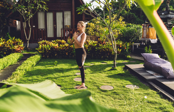 Side view of full body calm relaxed woman practicing yoga doing Vrksasana pose in green garden near small wooden house - Foto, Bild
