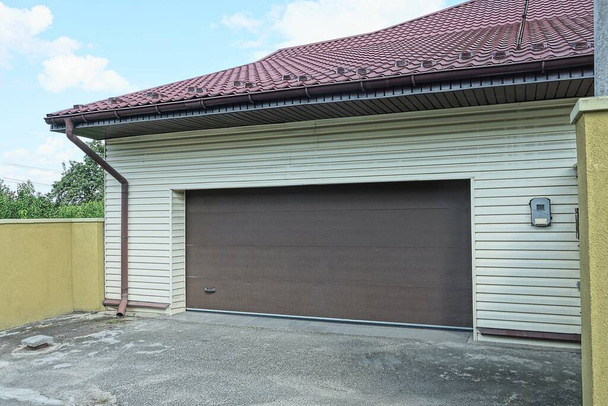 façade de garage gris avec portes brunes sous un toit carrelé dans la rue sur asphalte - Photo, image
