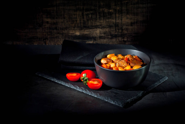 Yellow beans in a black bowl. Boiled beans with meat on a stone table. Beans with tomato sauce and pork. Contrasting dramatic light as an artistic effect. - Foto, Imagem