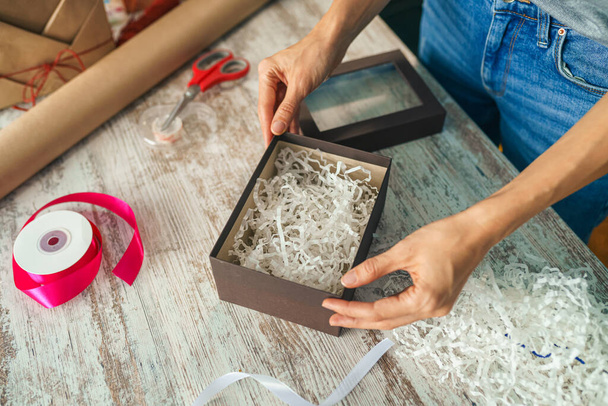 Woman putting kraft shredded paper in packaging box wrapping gift. Happy holiday present and gifts. DIY art craft - Foto, Imagem