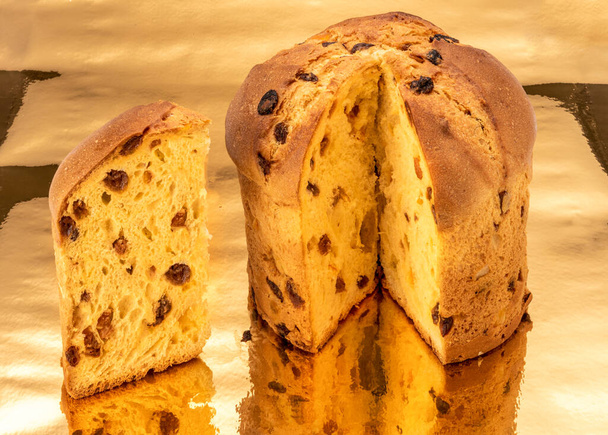 Panettone cake cut with slice on a golden background where it is reflected, classic Italian Christmas cake - Photo, Image