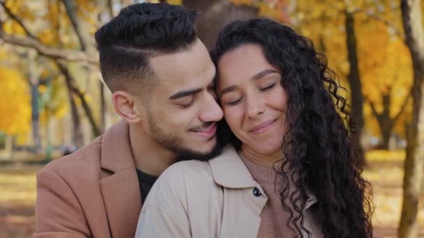Hispanic couple cuddling outdoors girl and guy on romantic date in autumn park family look into each other eyes lovers enjoy gentle embracing man and woman touching cheeks close-up beloved fun smiling - Footage, Video