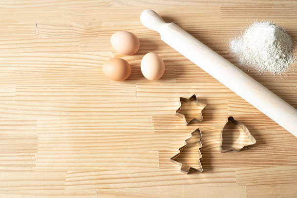 Házi készítésű karácsonyi sütik. Háttér fa munkaasztal. Görgőtű, keksz vágó, tojás. Sablon receptek.Másolás hely, Felülnézet, lapos fektetés - Fotó, kép