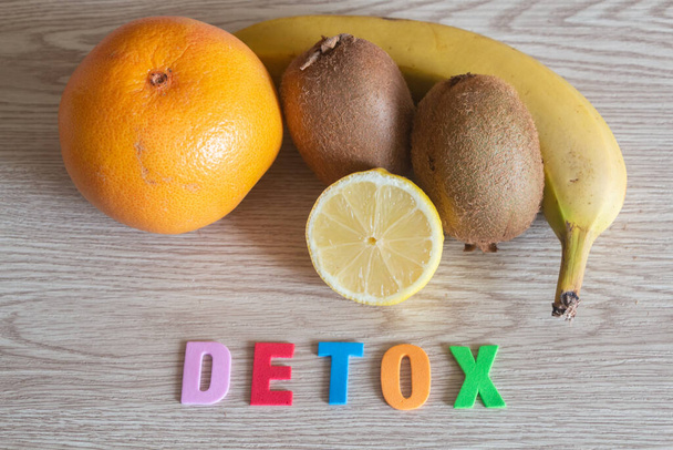 Grapefruit, banana, kiwis and half lemon with the word detox on wooden background - Foto, Imagem