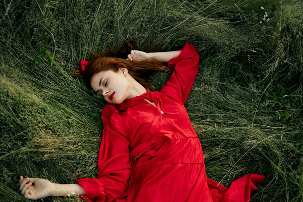 woman in red dress lies on the grass in the field nature landscape - 写真・画像