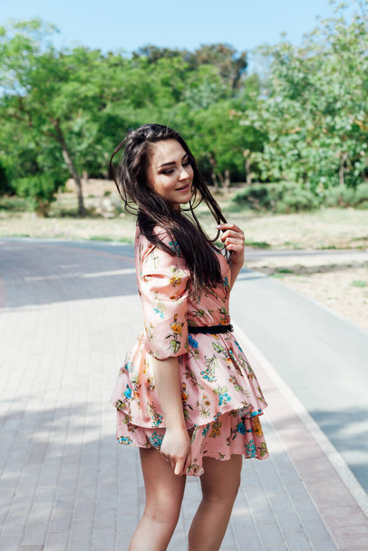 mooie brunette vrouw in een jurk met bloemen wandelingen langs de straat en het park - Foto, afbeelding