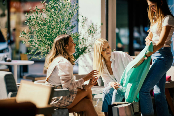 Trois boutiquiers sont assis dans un café et se montrent des vêtements qu'ils ont achetés pour une occasion spéciale. - Photo, image