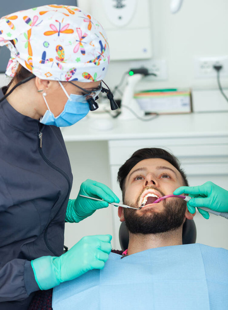 Žena zubní lékař vyšetřuje pacienta v zubní ordinaci pomocí profesionálních nástrojů a osobních ochranných prostředků. - Fotografie, Obrázek