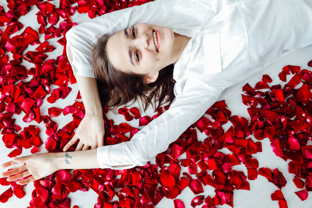 a beautiful woman lies in the petals of red rose flowers - Fotoğraf, Görsel