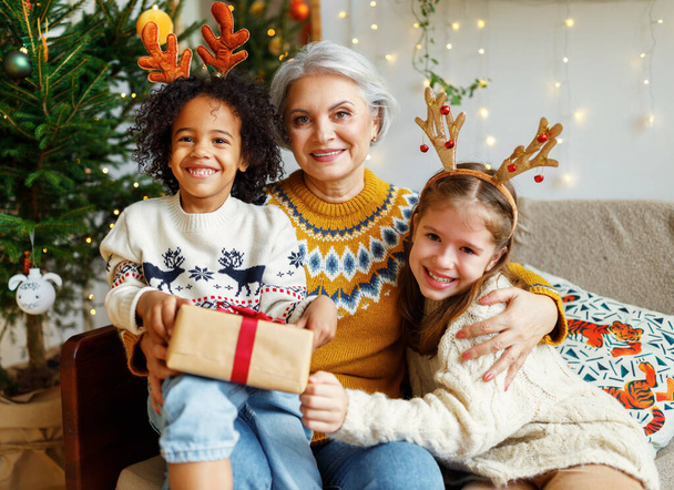 幸せな多人種家族シニア祖母とともにかわいい多人種間の子供クリスマスの朝自宅で - 写真・画像