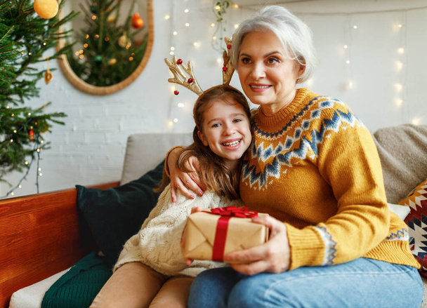 Klein meisje kleindochter geven kerst geschenkdoos aan glimlachende oma tijdens de wintervakantie - Foto, afbeelding