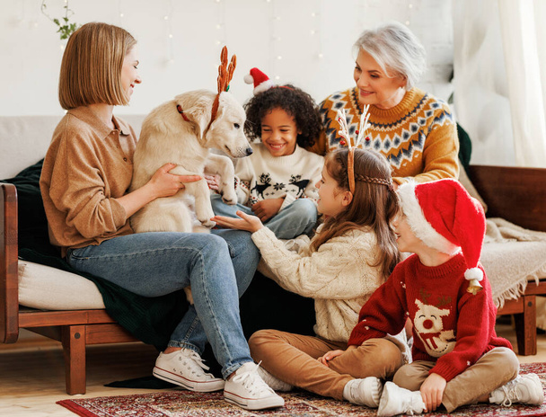Szczęśliwe dzieci coraz psa na Boże Narodzenie, wielonarodowa rodzina z golden retriever świętować Nowy Rok - Zdjęcie, obraz