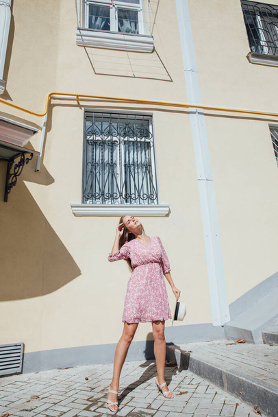 beautiful blonde woman in a summer pink dress walks around the city - Foto, afbeelding