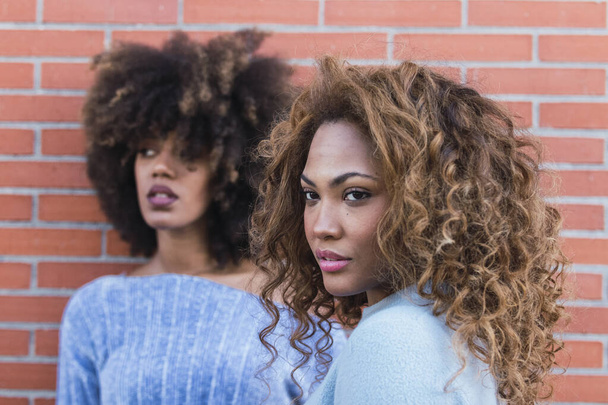 Vonzó afro-amerikai nők hosszú afro hajjal, csillogó sminkkel és kék pulóverrel, téglafalon pózolva. Szépség portré afrikai természetes lányok téglafalban. Szelektív fókusz - Fotó, kép