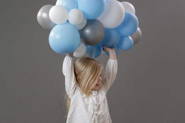 Studio ritratto di bambina felice che tiene un gruppo di palloncini bianchi e blu. Concetto di festa, felicità, desideri e speranze. - Foto, immagini