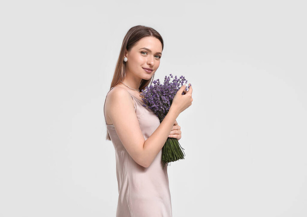 Beautiful young woman with bouquet of lavender on light background - Foto, afbeelding