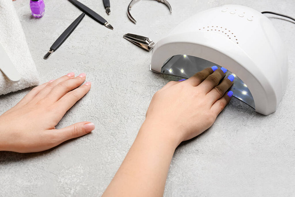 Mani femminili e lampada per asciugare lo smalto gel su tavolo leggero - Foto, immagini