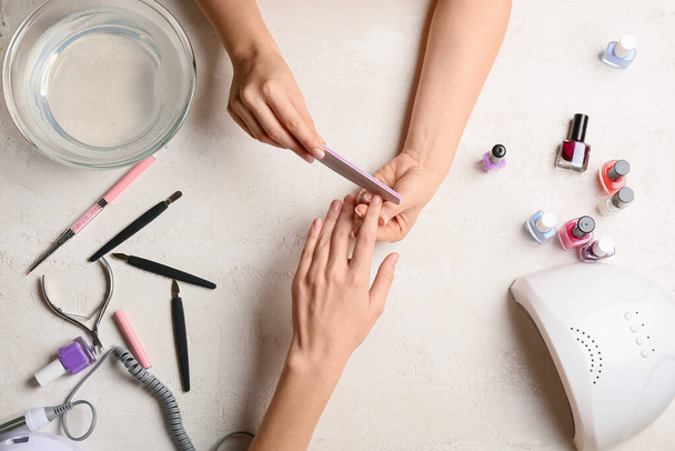 Manicure master filing nails to female client on light table - Fotó, kép