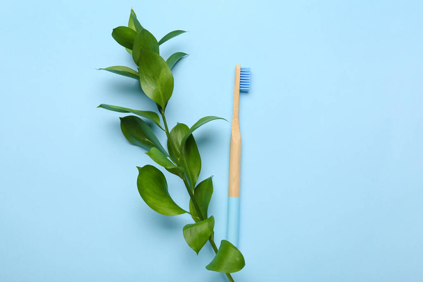 Spazzolino da denti in legno e ramo vegetale su sfondo blu - Foto, immagini
