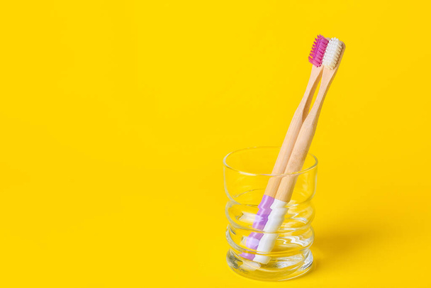 Vidrio con cepillos de dientes de madera sobre fondo amarillo - Foto, imagen