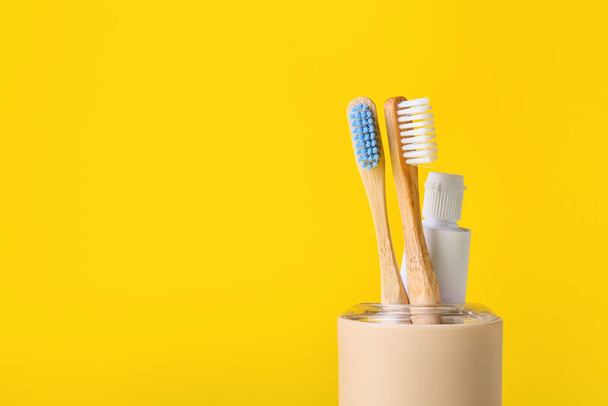 Holder with wooden toothbrushes and paste on yellow background, closeup - Photo, Image