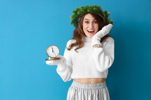Giovane donna sorpresa in abiti invernali, con corona di Natale e orologio su sfondo a colori - Foto, immagini