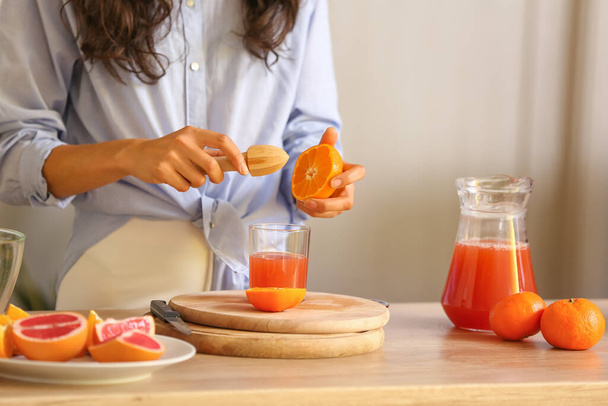Young woman making fresh citrus juice in kitchen - Foto, Bild