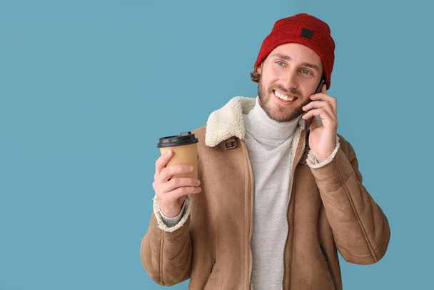 Handsome man with coffee talking by mobile phone on color background - Valokuva, kuva