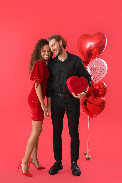 Glückliches junges Paar mit Geschenk und Luftballons auf farbigem Hintergrund. Valentinstag-Feier - Foto, Bild