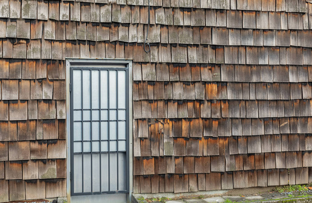 Podrobnosti o staré stodole na venkově. Rustikální nástěnné vzory ošlehaného cedru otřásají šindele s dveřmi ve venkovské oblasti. Pohled do ulice, selektivní zaměření, nikdo - Fotografie, Obrázek