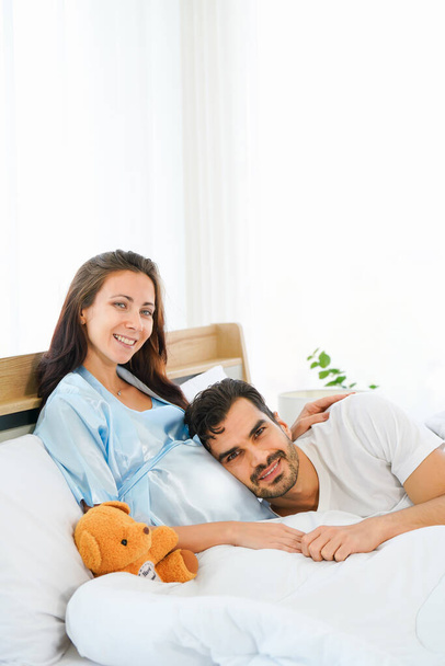 portrait of happy pregnant wife and husband lying together on bed in bed room at home - Foto, immagini