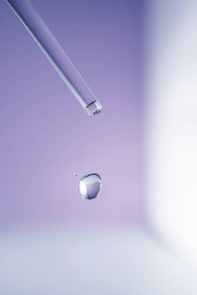 A drop of cosmetic oil falls from the pipette on a purple floral background. - Photo, image