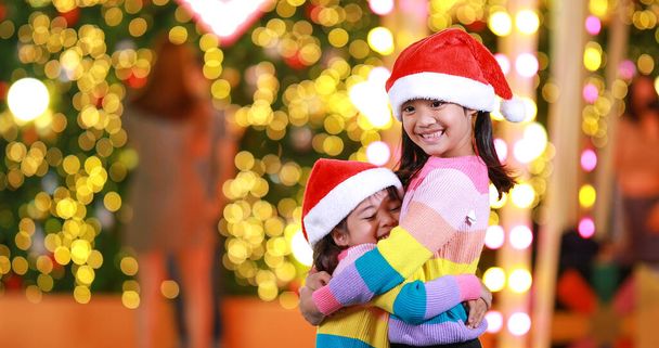 Nouvelle année anticipation.Deux mignonne petite fille Portant un chapeau de Noël rouge et belle chemise de couleur sur un fond de Noël avec des lumières bokeh. Amusez-vous et amusez-vous pendant cette saison importante. - Photo, image