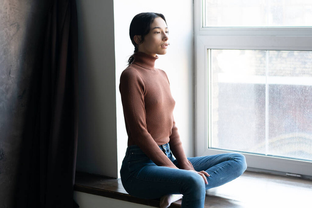 young beautiful woman sits in jeans near the window in the studio - Foto, Bild