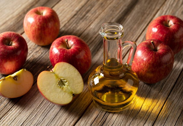 Apple vinegar in a glass container against a wooden background with lots of apples around it. - Photo, image
