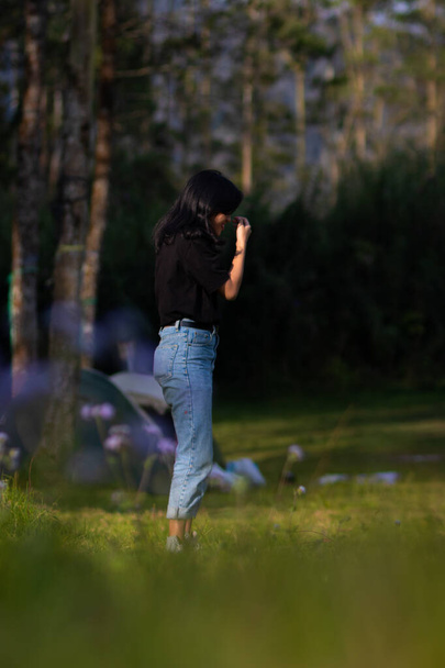 Relaxační dívka s modrými džínami stojí na zelené trávě s kvetoucími květinami a zároveň se dotýká jejích vlasů - Fotografie, Obrázek